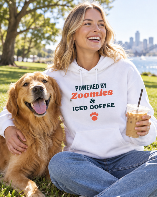 Smiling woman with her Golden Retriever in a sunny Sydney park, wearing the white Powered by Zoomies & Iced Coffee hoodie (AI-generated image)